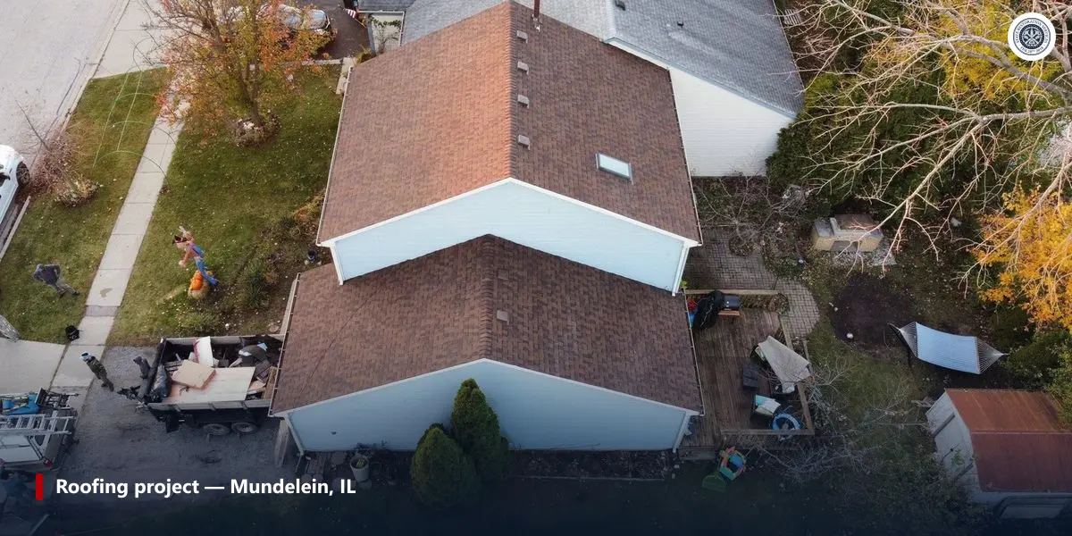 Aerial view of a completed asphalt shingle roof replacement in Mundelein, Illinois, with the tear-off trailer in the drive