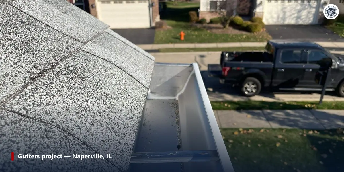 Inside of a seamless aluminum gutter at a sealed joint beside asphalt shingles on a completed Naperville, Illinois project
