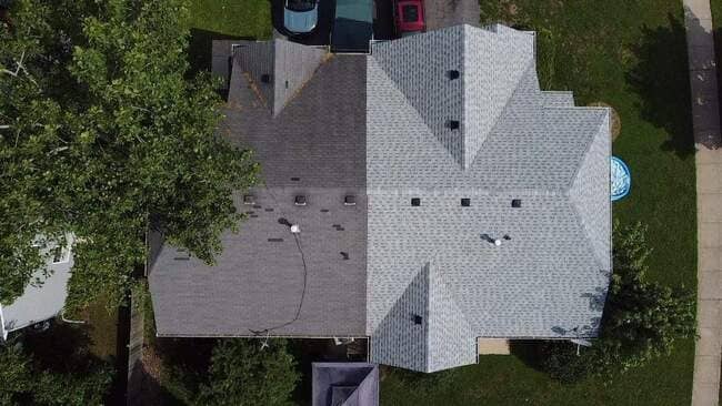 Top-down aerial drone view of a residential home roof undergoing a roof replacement, showing a distinct split-screen contrast between the old dark gray asphalt shingles on one side and the newly installed light gray architectural shingles on the other.