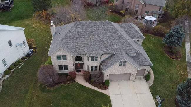 Aerial overhead view of a completed residential asphalt shingle roof featuring clean architectural lines, precise hip and ridge caps, and integrated roof vents. The professional roofing system demonstrates durable, high-quality installation standards.