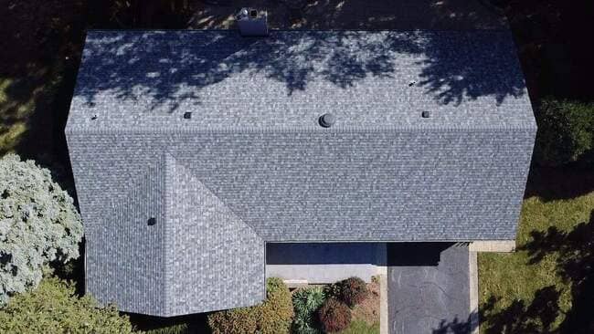 Aerial overhead view of a completed residential asphalt shingle roof featuring clean architectural lines, precise hip and ridge caps, and integrated roof vents. The professional roofing system demonstrates durable, high-quality installation standards.