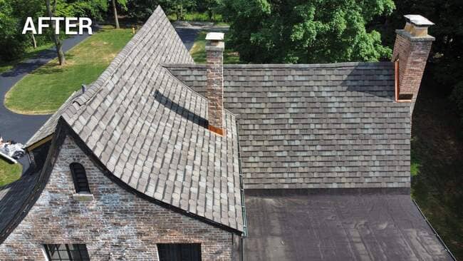 Aerial drone view labeled "AFTER" showing a newly installed gray slate-style shingle roof on a Tudor-style brick home with two brick chimneys, copper flashing, and a flat roof section.