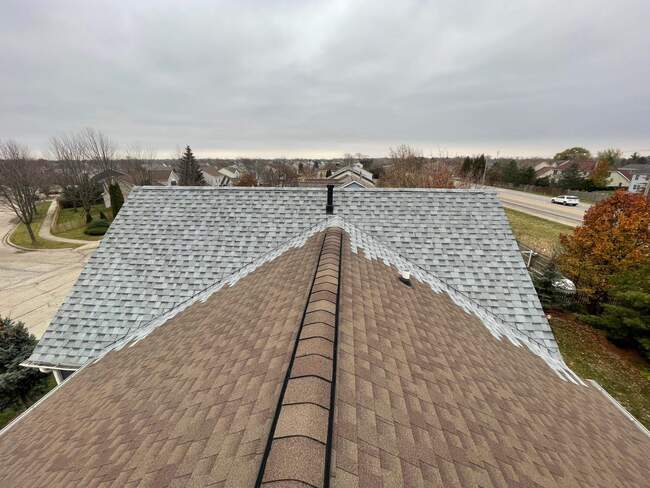 Rooftop perspective of a residential home during a roof replacement, showing a distinct transition between brown architectural shingles in the foreground and older gray asphalt shingles in the background against an overcast sky.  3. Helpful, Keyword-Rich Caption for Yelp (M