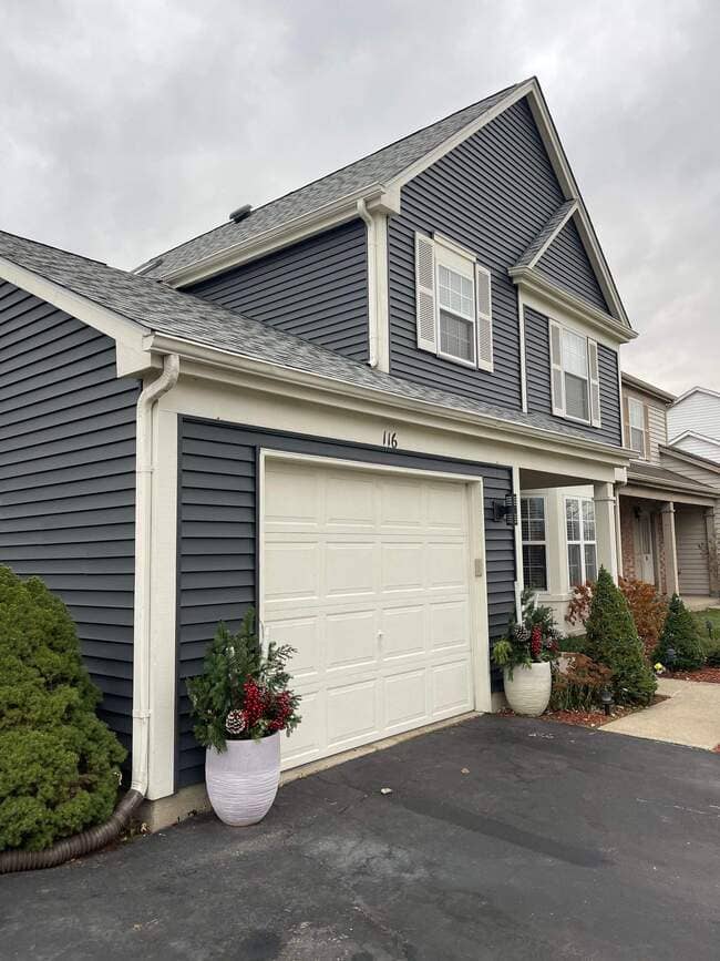 Exterior view of a two-story home with dark gray siding, white garage door, white window shutters, and a newly installed light gray architectural shingle roof under an overcast sky.