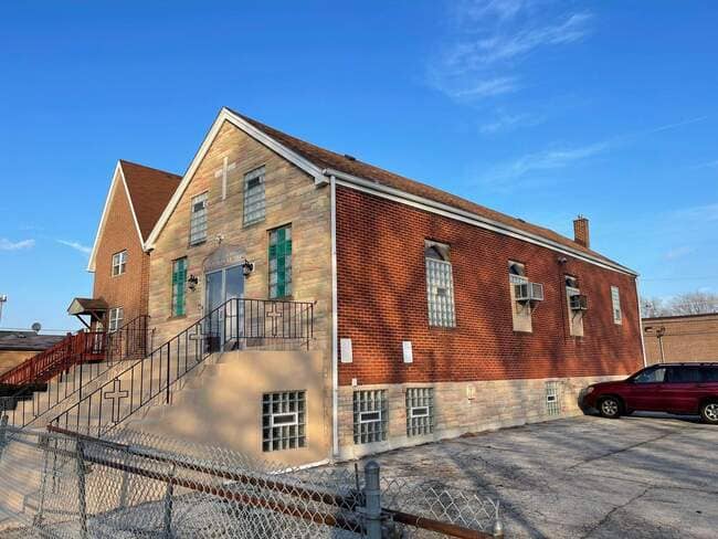 Exterior front and side view of a brick church building featuring a stone front facade, wrought iron railings on front steps, glass block windows, and a newly installed brown shingle roof under a clear blue sky.