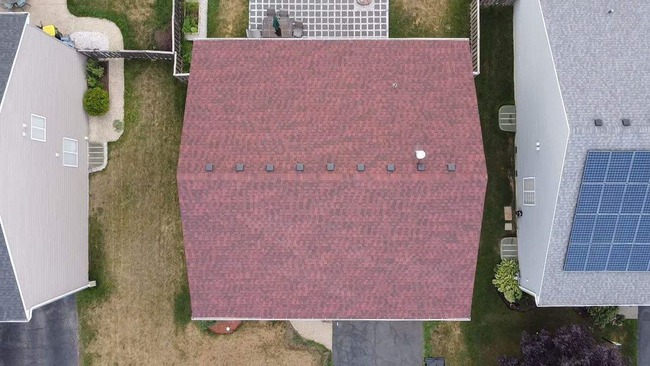 Aerial view of residential roofing project featuring red asphalt shingle roof with multiple vents, surrounded by neighboring homes with light and gray roofs, one with solar panels - professionally installed for durability and curb appeal
