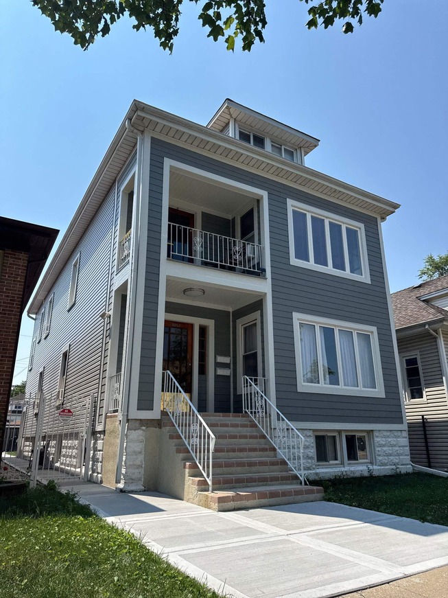 Exterior view of two-story house with grey horizontal vinyl siding, white corner trim, white window casings, covered front porch with white railings, and upper balcony—professionally installed siding for enhanced curb appeal and durability